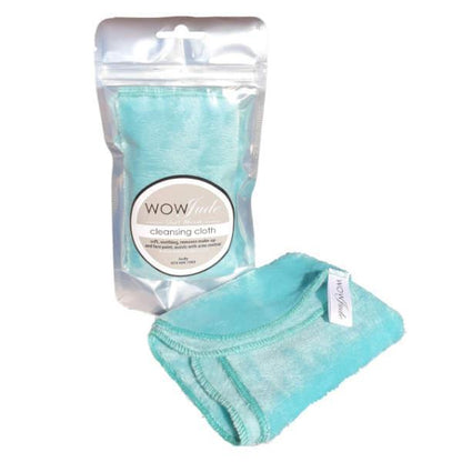 A light blue WOW Jude Face Cleansing Cloth is displayed in front of its packaging. The packaging is a silver foil bag with a clear window, showing a similar cloth inside. Both cloths appear soft, with stitched edges, and each has a white tag with the brand name. Perfect for acne-prone skin.